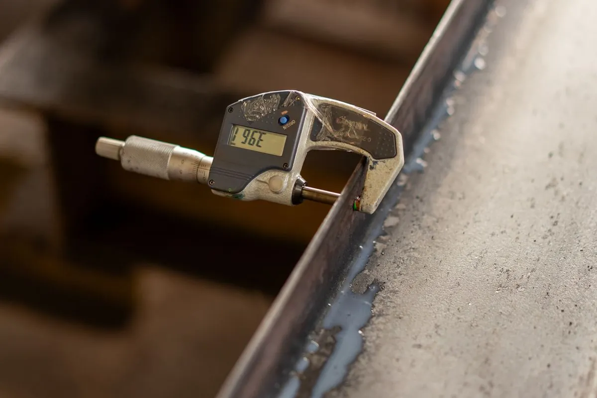 Stock photograph of a digital micrometer measuring the thickness of a metal edge; not Omita inspection equipment.